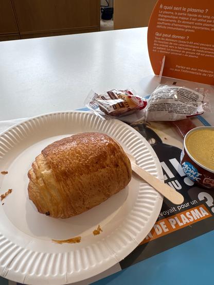 Une chocolatine dans une assiette en carton, avec une crème chocolat et une madeleine