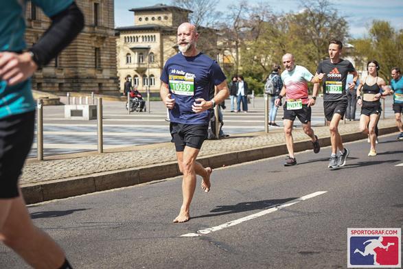 Barfußläufer in einer Gruppe mit anderen Sportlern bei Sonnenschein in der Leipziger Innenstadt mit dem Gebäude des Bundesverwaltungsgericht im Hintergrund