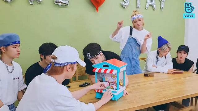 skz members sit around a table playing games. Hyunjin stands up and does a silly dance