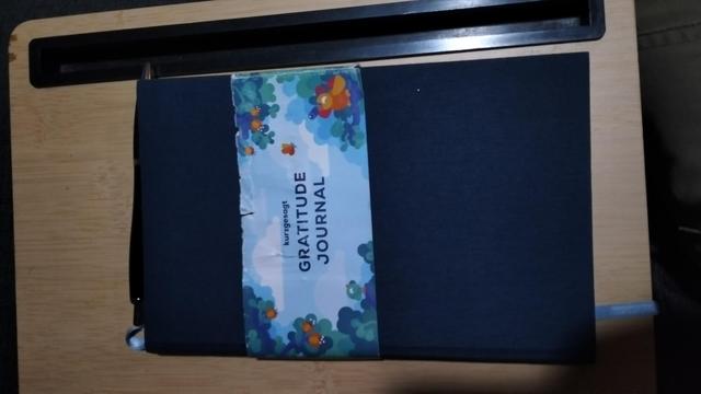 Cover of gratitude journal. It still has the decorative paper strip around it, but that strip is now damaged from 15 months of having a pen put on and pulled off.
