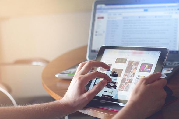 Handen bij een iPad met op de achtergrond een laptop. Afbeelding van fancycrave1 via Pixabay