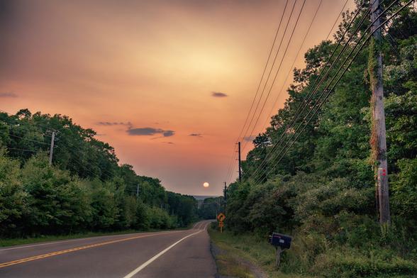 color photograph taken on Route 6 PA of a sunset over the road tinged with wildfire smoke giving it a strange orange glow