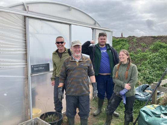 Four smiling people standing in front of a polytunnel