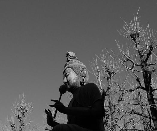 A black and white photo of a buddhist statue with bare decorative trees behind it.