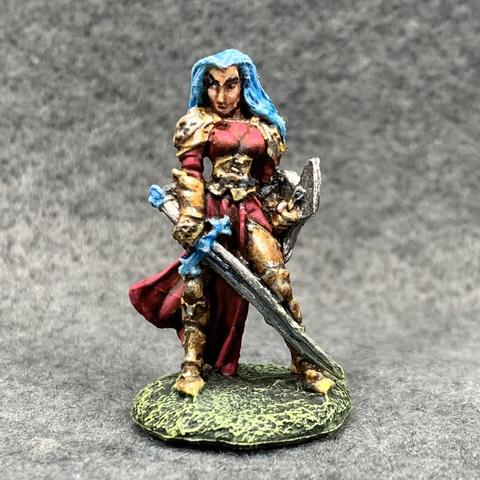 Person in plate mail and a red robe under the armor and bodice. They hold a long silver sword and shield. They have long blue hair and a judgy, skeptical look.