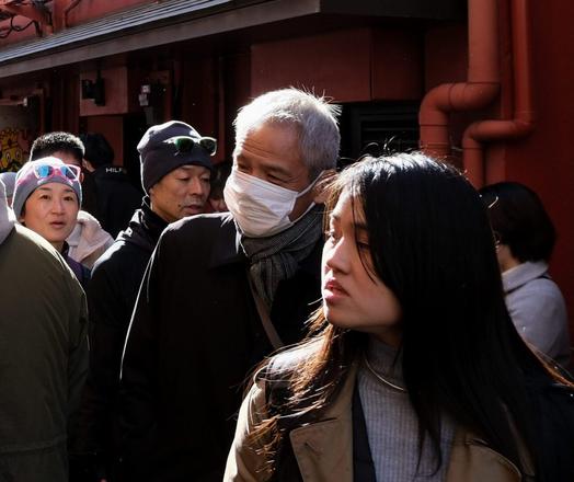 People in a crowded lane near Sensoji Temple, Tokyo. Those in the foreground are looking towards a stall to the left out of frame, while a woman behind them looks directly at the camera.