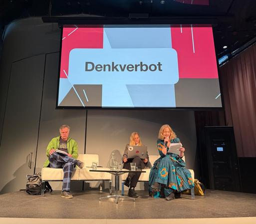 Die drei genannten Personen auf der Bühne, dahinter ist auf einer Videoleinwand "Denkverbot" zu lesen. Evelyn Schalk hat das Mikrophon.