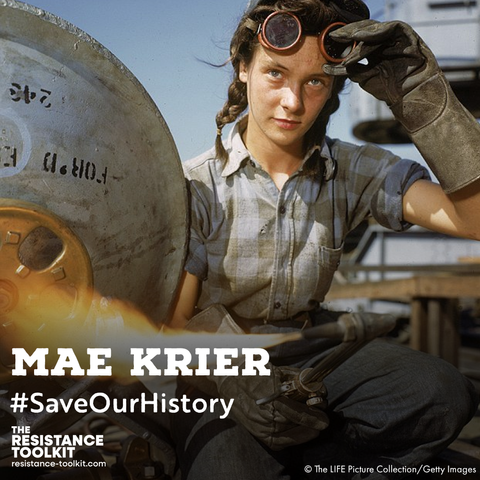 A vintage photograph of a young Mae Krier during World War 2. She is pulling up her welding googles to look out at the camera while her welding torch shoots out a flame.