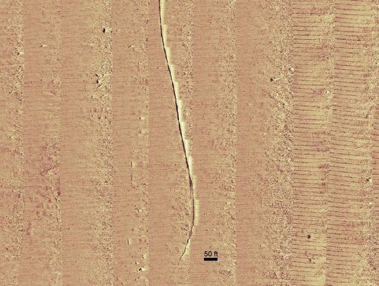Gold-tone mosaic sonar image with dark line (pipe) & adjacent shadow (light).