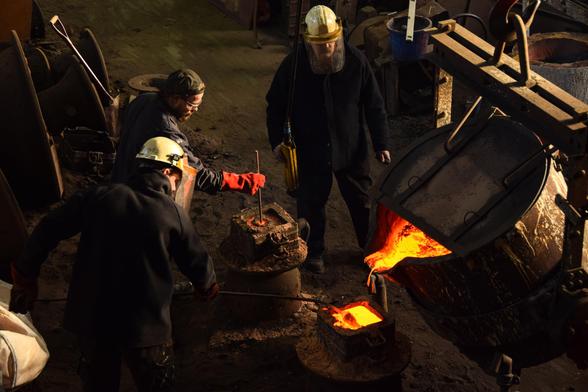 Workers pouring hot bell metal into the mould that is buried in the sand.