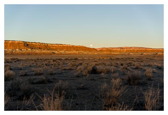A small moon really close to the top of some cliffs in the distance, during the morning golden hour so the cliffs are lighting up as the floor is still dark