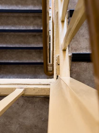 Alt Text von ChatGPT

Das Bild zeigt ein Treppenhaus das von oben nach unten aufgenommen wurde.
Man sieht ein Geländer in einem gelblichen Farbton sowie Stufen mit einer grauen Oberfläche und schwarzen Trittleisten.
Die Linien des Geländers und der Stufen erzeugen ein geometrisches Muster. Die Perspektive und der Bildausschnitt verleihen dem Foto eine abstrakte Anmutung.