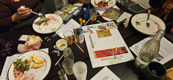 Plates of almost finished dinner being eaten. There are empty glasses and an in-progress collage on a black table.