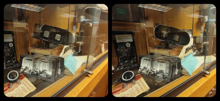 A display case filled with stereoscopes, ViewMasters, 3D cameras, etc. There's a lot of reflection on the glass.