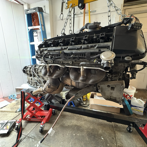 A view of the right-hand side of my BMW M54B30 inline-six cylinder engine, hanging from a hoist in my garage, with newly reinstalled exhaust manifolds with new gaskets and heat shields.