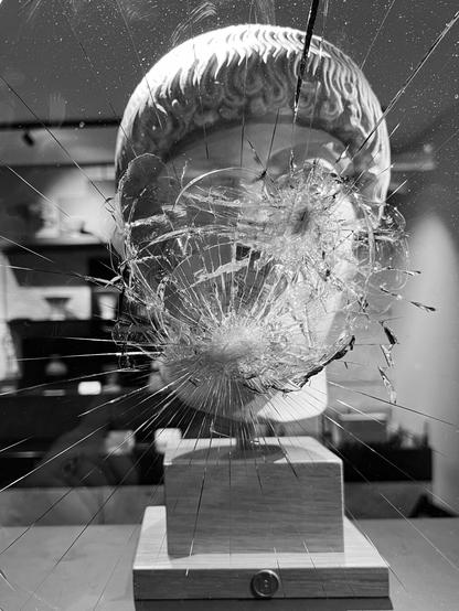 A shattered star of safety glass, the window of an expensive museum shop next to Syntagma Sq in Athens. Behind it, the reproduction of a marble head of a young man. The shatter pattern obscures his features.