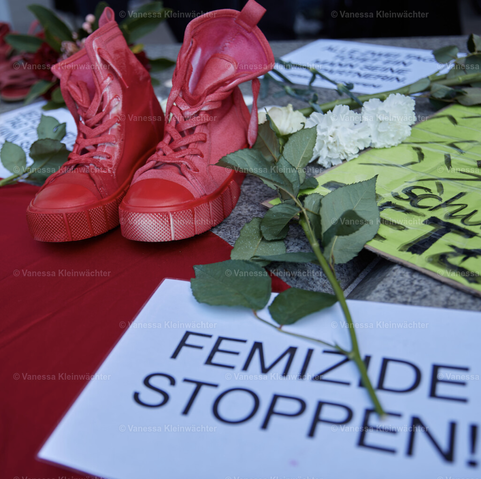 Ein rotes Paar Sneaker und weiße Blumen, daneben ein Schild: "Femizide stoppen!"