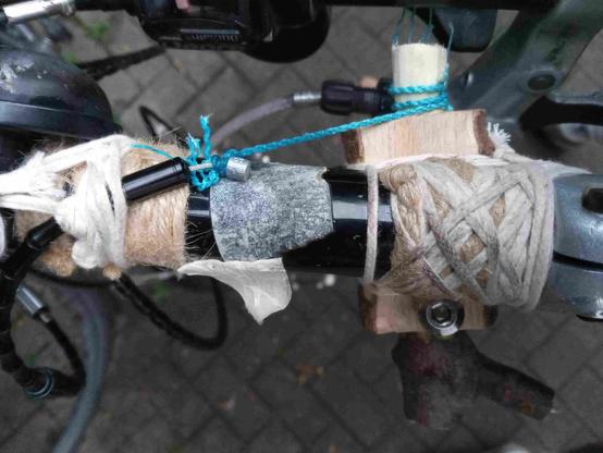 Manette de vitesses en noeuds, en bois, en coton, en dyneema, avec une vis en acier aussi...

L'idée est de bloquer la gaine en perles d'alu avec un noeud constricteur, de tirer sur le cable avec le même nœud fixé à la tête de câble d'une part et à une branche taillée et percée de l'autre. Percée pour permettre d'enrouler comme pour une bobine le fil tirant le câble.
La branche fourchue taillée et percée tourne et frotte pour enrouler le câble de dyneema tirant sur le câble inox de vitesse.
 Frotte dans un énorme trou (gros comme l'épaisseur d'un doigt), et cette friction est régulée par une vis métallique se mettant dans un taraudage appuyant sur la branche bobine.
Ça ressemble un peu à un boîtier de pédalier de vélo avec son axe, qui frotterait pour enrouler du fil.
Cette manette est attachée à un levier de frein VTT fixé sur un prolongateur long  un peu comme ceux du triathlon.