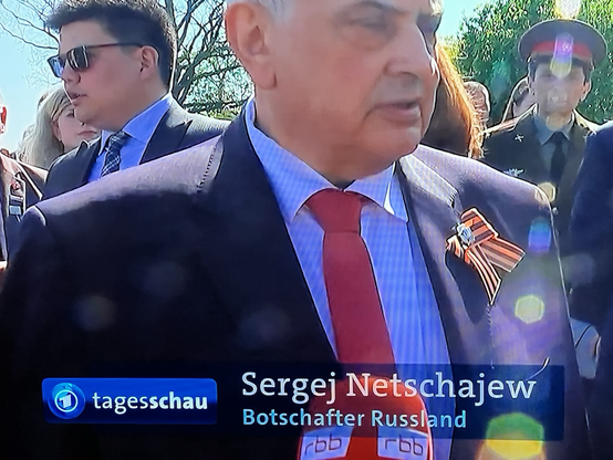 Ein Ausschnitt der heutigen Tagesschau abfotografiert: Ein wichtiger Mann mit Krawatte, dahinter weitere Leute. Auf der Bauchbinde neben Logo und Schriftzug der Tagesschau steht „Sergej Netschajew. Russischer Botschafter“.