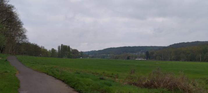 Vue d'un paysage de campagne, au premier plan une piste cyclable, ensuite un champs tout vert et au fond une voie de chemin de fer
