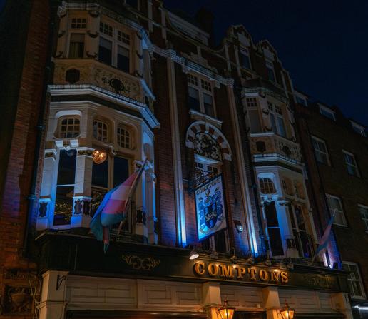 Night photo of a pub called Comptons flying two Trans Pride flags.