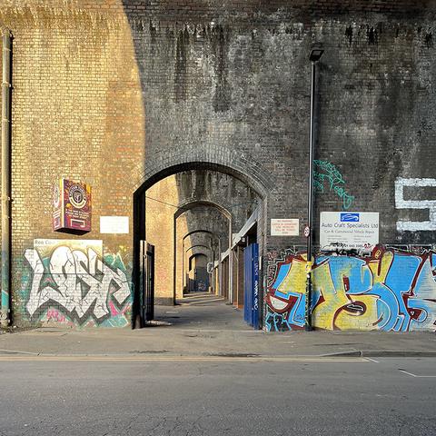 A beautifully textured, industrial brick wall - possibly Victorian - in Birmingham. The brick is a yellowish tone, stained as if by tainted water running down from the top of it. The wall is graffitied at the bottom - yellow and blue on the right, white with a black drop-shadow on a multicoloured background on the left, with industrial-looking signage. There's an elegantly shaped segmental arch opening, through which we can see a series of similar openings in walls further away, the perspective showing the archways diminishing in size so that those further away seem to be contained by the ones closer to the viewer.