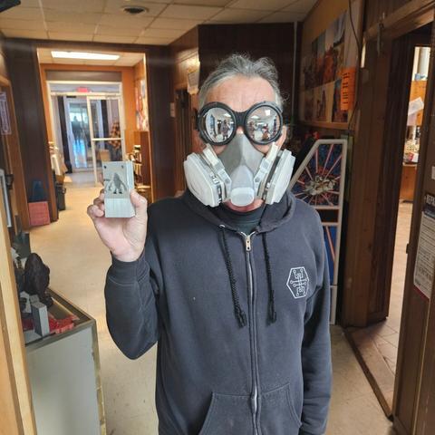 a photo of me, wearing reflective (not laser safe!) goggles, a respirator mask, and a hackers.town hoodie that has little bits of aluminum all over it as I hold up one of the mold halves I just took an angle grinder to to get it flattened out appropriately.