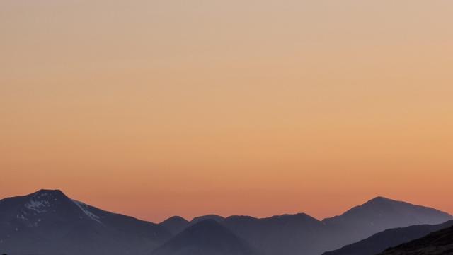 An orange sky at sunset with mountains silhouettes along the lower quarter of the frame.