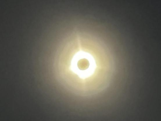A solar eclipse is depicted, with the moon partially blocking the sun, creating a bright ring-like effect around the darkened center. The surrounding area has a gradient of light.
