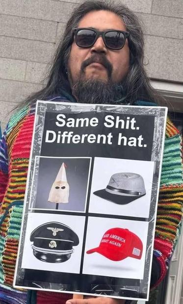 Man in colorful sweater holding a sign that reads:  "Same Shit. Different hat." above a four quadrant photo display of a KKK hood, a Confederate infantry cap, a Nazi officer hat and a red MAGA ballcap.