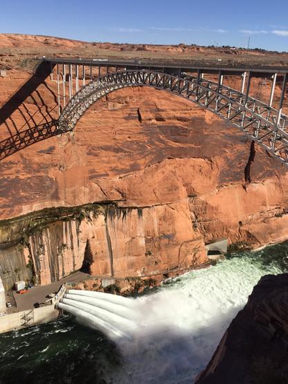 Water bursts out of the bottom of Glen Canyon Dam from a viewpoint high above the Colorado River.
