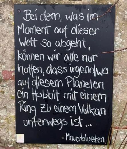 Eine schwarze Tafel an einer Wand, auf der steht:"Bei dem, was im Moment auf dieser Welt so abgeht, können wir alle nur hotten, dass irgendwa auf diesem Planeten ein Hobbit mit einem Ring Zu einem Vulkan unterwegs ist ..."
Von
 Mavertolueten