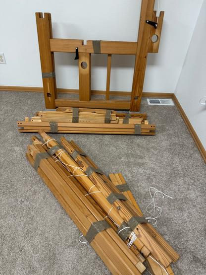 a bunch of wooden parts of a swedish floor loom , taped up with grey packing tape.