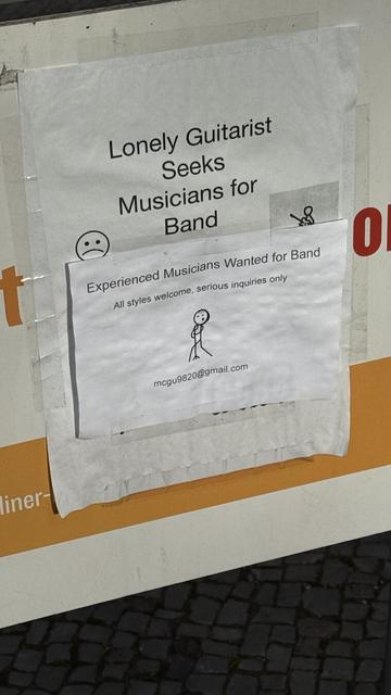 Sign „ Lonely Guitarist Seeks Musicians for Band“ with another sign taped over: „Experienced Musicians Wanted for Band. All styles welcome, serious inquiries only mcgu9820@gmail.com“