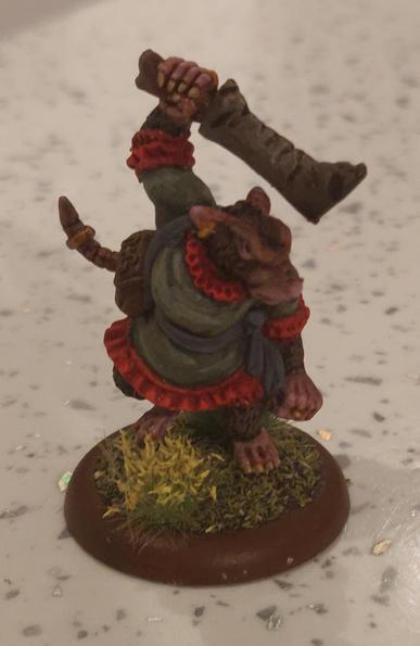 We have a 28mm model of an anthropomorphic rat wearing a green dress with red frills. She's angrily facing right with a machete wielded above her head.