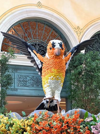 A large colorful parrot sculpture in a flower garden.
