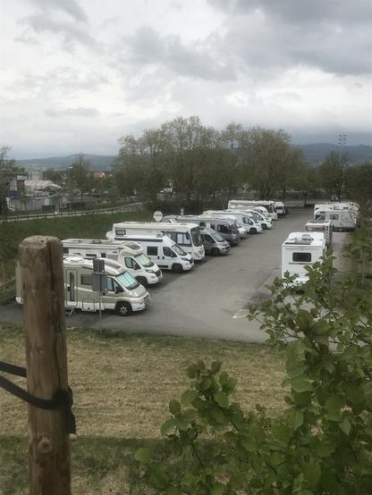 Foto von einem Wohnwagenstellplatz, auf dem mehrere Wohnmobile stehen. Foto von einer erhöhten Stelle aufgenommen. Im Hintergrund Berge im Nebel und ein bewölkter Himmel.
