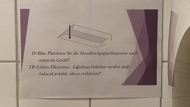 Sign reading: D-Bitte Platzieren Sie die Handlöschpapierbiegeseite nach
unten im Gerät!!
TR-Lütfen Elkurutma kagidinin bükülme tarafini asag
bakacak sekilde cihaza yerles tirin!!