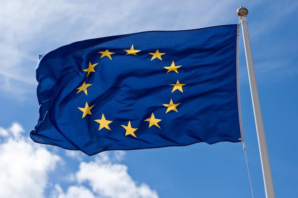 Een wapperende Europese vlag met wolken en een blauwe hemel op de achtergrond.