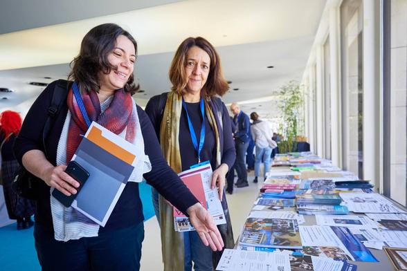 Cláudia Ninhos with other female participant in the Civil Society Forum on Combating Anti-Semitism next to a table with leaflets. Photo by Christophe Licoppe.