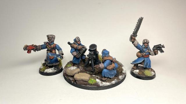 A Valhallan leader model with bolt pistol and power sword, a mortar team and a valhallan squad leader on a white background. Their uniforms are painterly blue with brown accents.