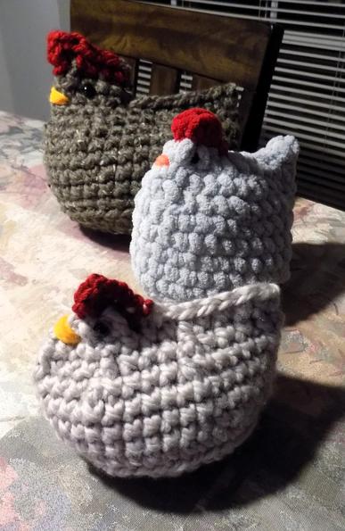 On my kitchen table, three crocheted emtional support chickens in tan, gray and medium brown tweed yarns with red yarn combs and yellow and orange embroidered beaks.