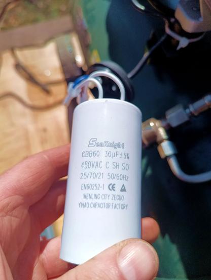 Close-up of a large white motor run capacitor popped out of its black housing underneath the compressor pump. The cables are still attached. The label reads SeaKnight CBB60 30μF 450V.
