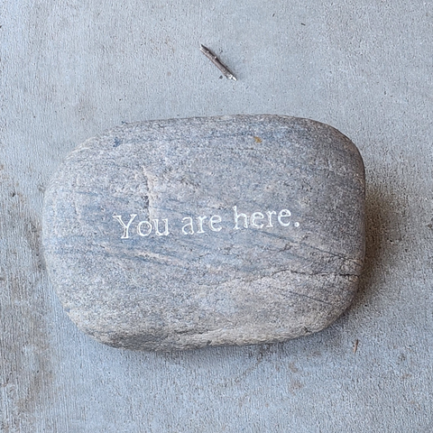 color photo of a large stone gray on gray background, words etched in the stone read, "you are here."