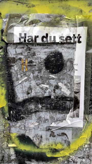 En opprinnelig grå flate (strømboks) med noen tykke streker tagging i svart og en stor prikk. En gul tykk taggestrek, rundt (følger stort sett bildekanten). Inni denne et A4 ark der det meste er klippet/revet vekk, bortsett fra øveste del og høyre. Øverste del har teksten "Har du sett" i tykke svarte bokstaver. Rester av et svarthvitt bilde og litt tekst på høyre rest. Overflaten er bortsett fra taggingen, full av rester av papir, skit, skraper osv. Grov tekstur.