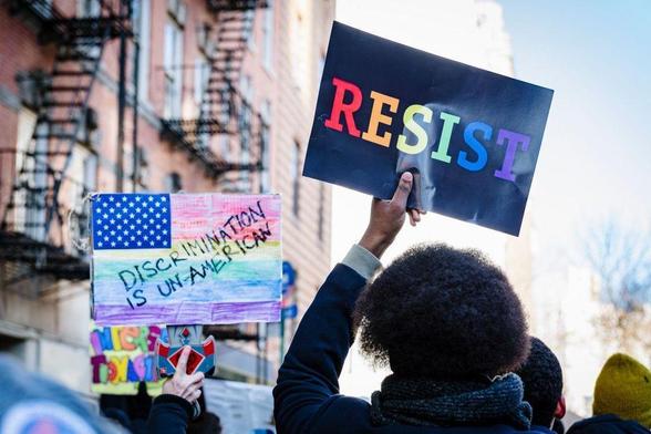Protesters carry signs in New York City saying, "Resist!" and "Discrimination is Un-American" reflecting American protests against systemic racism and discrimination