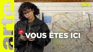 Capture du reportage de Tracks. Une journaliste est dans un couloir du métro, elle consulte son téléphone portable dubitativement. Derrière elle, un plan géant du métro de Paris.
