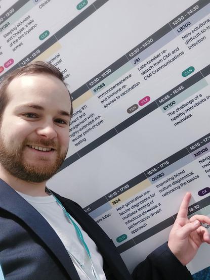 Scientist Mirko Sonntag is pointing on a schedule where his talk is presented in a list with other talks.