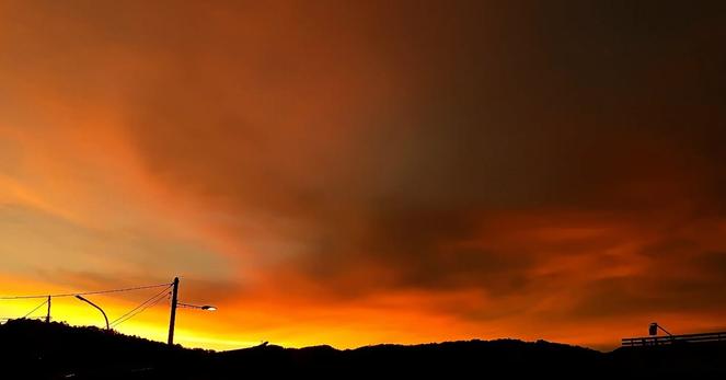 The sun sets behind the hill, it's remaining light burn the clouds orange as darkness creeps in from above.
