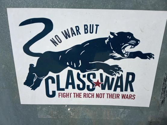 A graphic in black on a white background. Above the silhouette of a jaguar the lettering: “”NO WAR BUT...” below the big cat: ‘CLASS WAR’. A red star between “CLASS” and “WAR”. Underneath in red: “FIGHT THE RICH NOT THEIR WARS”.